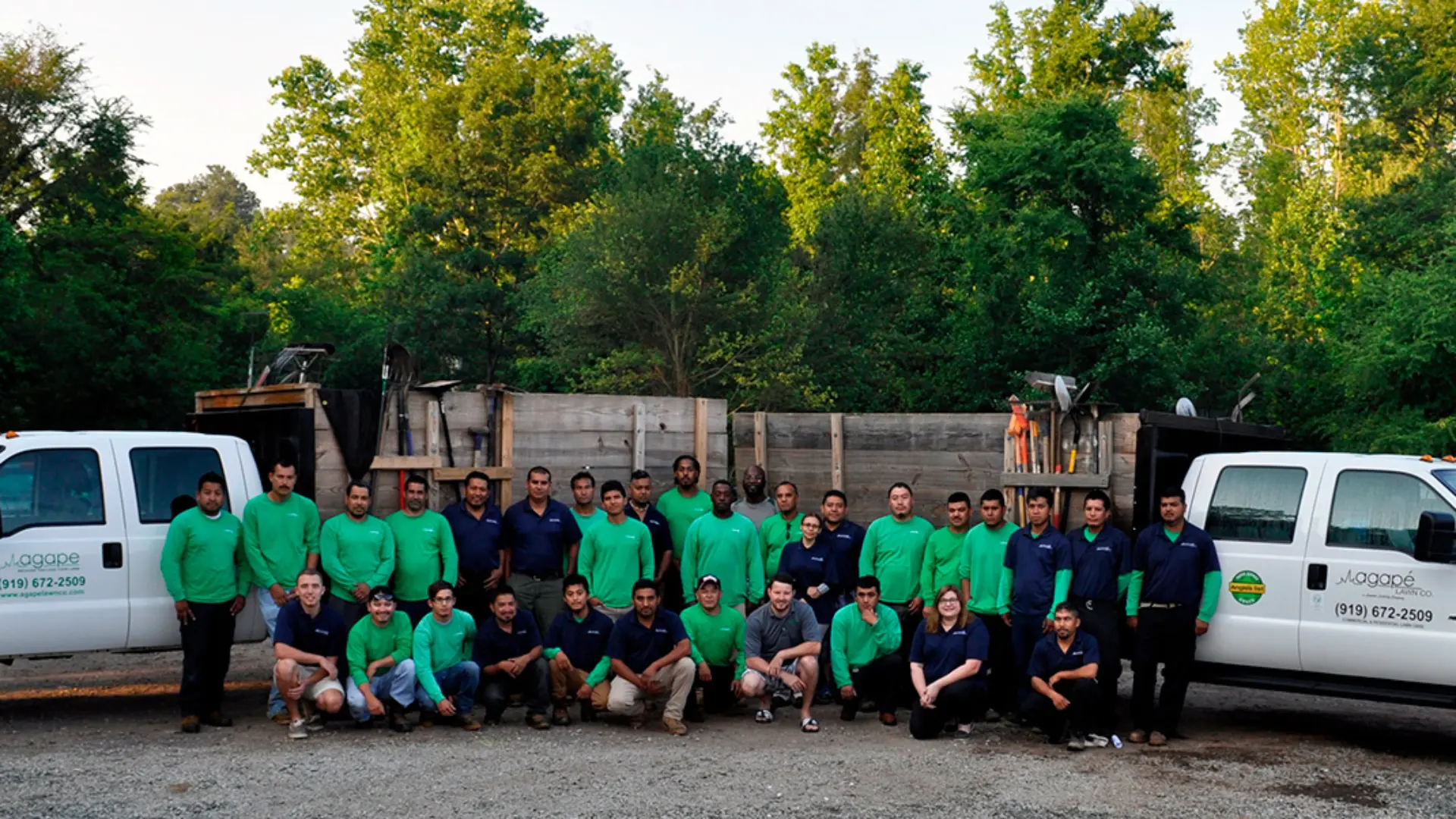 Agape Lawn Company team in front of work trucks with green trees in the background.