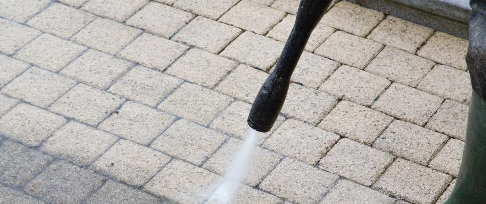 Person pressure washing a paver patio.