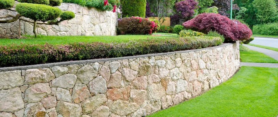 Retaining wall in Cary, NC, with shrubs and flowers by a green lawn.